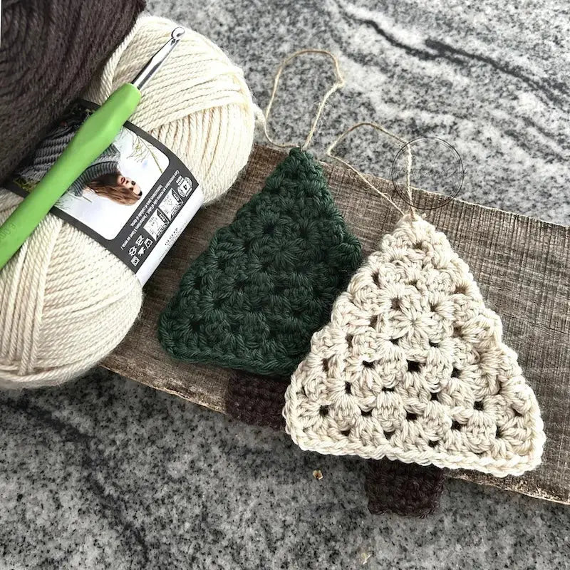 The ornaments, made from this crochet pattern, are lying on a wooden board with yarn and a crochet hook.