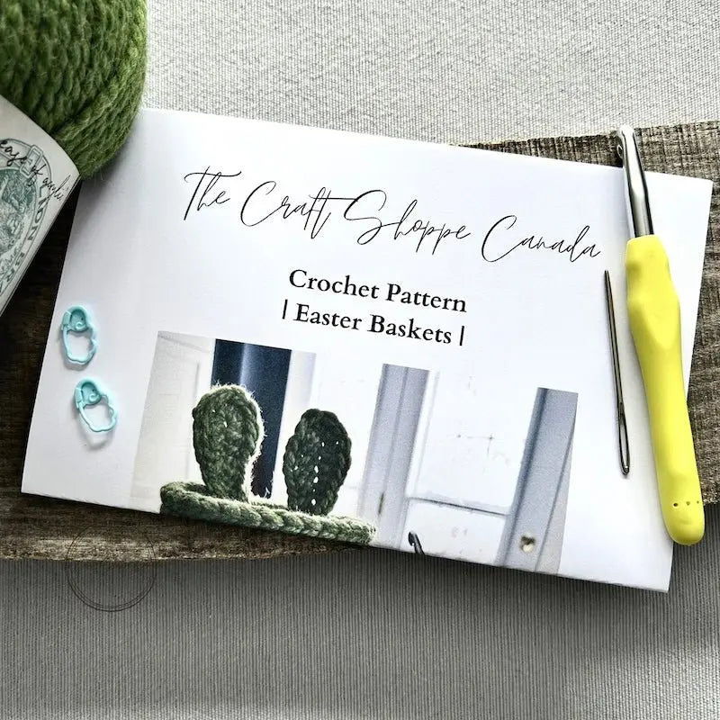 The pattern is lying on a wooden board with yarn, a crochet hook, a tapestry needle and 2 stitch markers.