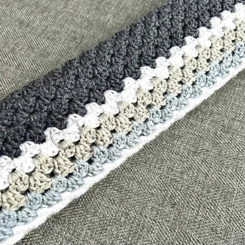 The finished granny square blanket, made from this crochet pattern, is lying across a couch.
