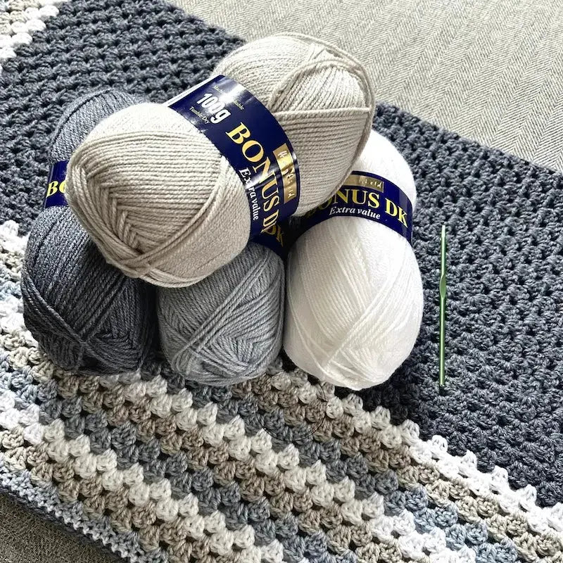 The finished granny square blanket, made from this crochet pattern, is lying on a couch with 4 balls of yarn.