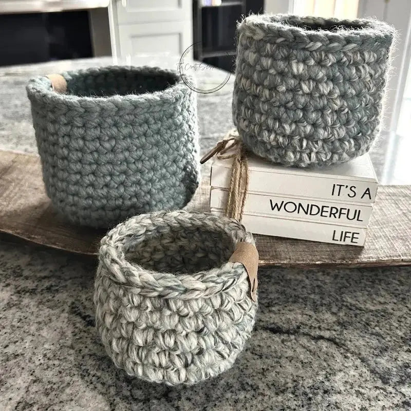 The storage baskets, from this crochet kit, are sitting on a wooden board on top of a counter.