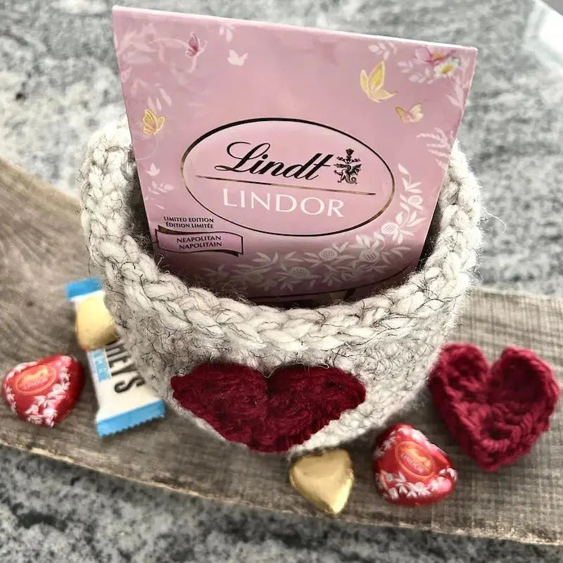 A close up of the heart basket, sitting on a wooden board, with chocolates inside and out of the basket.