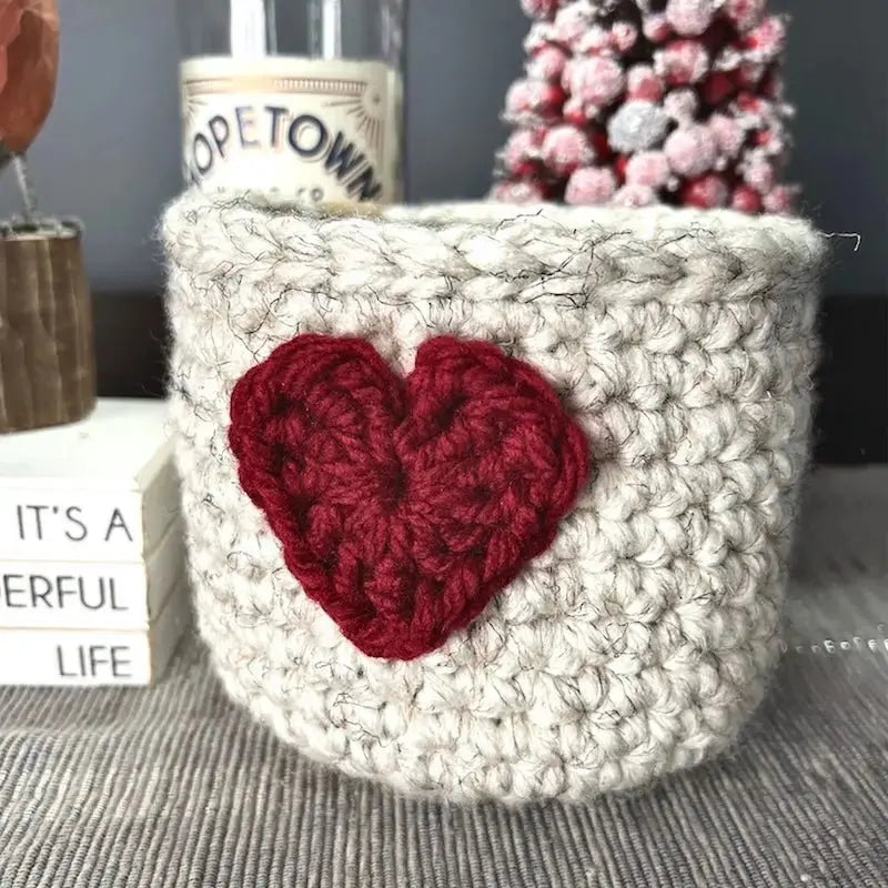 The heart basket, from this crochet kit, is sitting on a buffet with a spring bird beside it.
