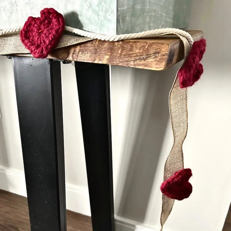 A finished section of the heart garland, made from this crochet pattern, is hanging over a table.