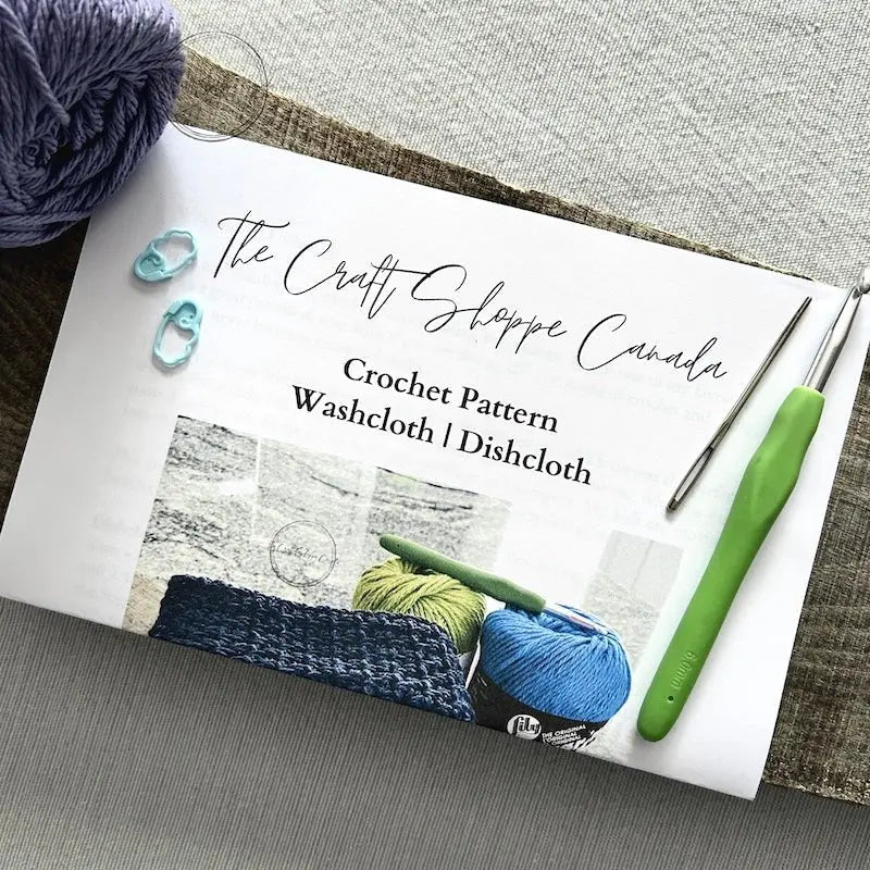The crochet pattern is lying on a wooden board with yarn, a crochet hook, a tapestry needle and 2 stitch markers.