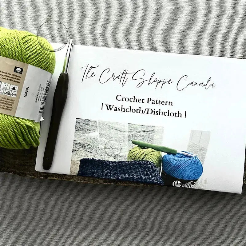 The pattern for this crochet kit is lying on a wooden board with yarn, and a crochet hook.