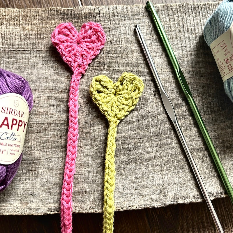 The finished bookmarks, made from this crochet kit, are lying on a board with yarn and crochet hooks.