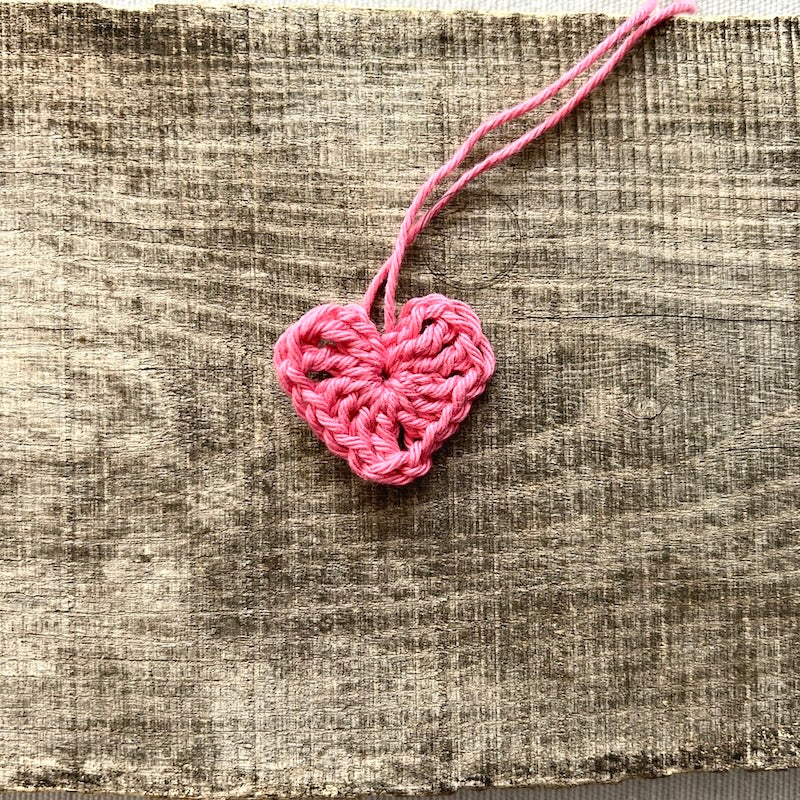 A pink heart, made from this crochet kit, lying on a board.