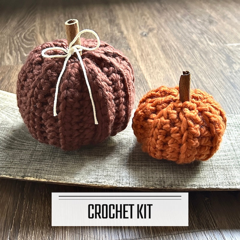 A crochet kit for a set of autumn pumpkins. The finished pumpkins are sitting on a wooden board.