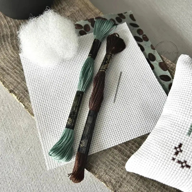 The supplies included in your cross stitch kit are sitting on a wooden board.