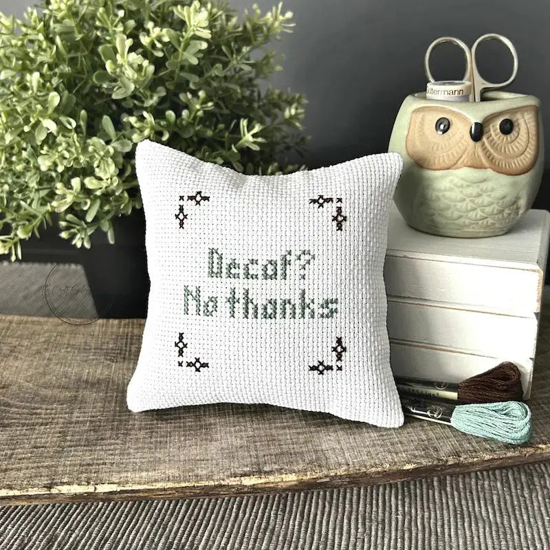 The finished pillow, made from this cross stitch kit, is sitting on a wooden board.