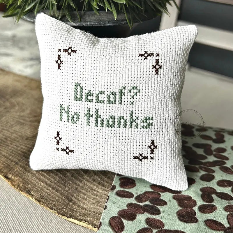 The finished pillow, made from this cross stitch kit, is sitting on a wooden board.