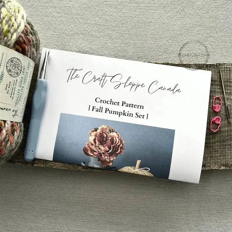 The pattern is lying on a wooden board with yarn, a crochet hook, a tapestry needle and 2 stitch markers.