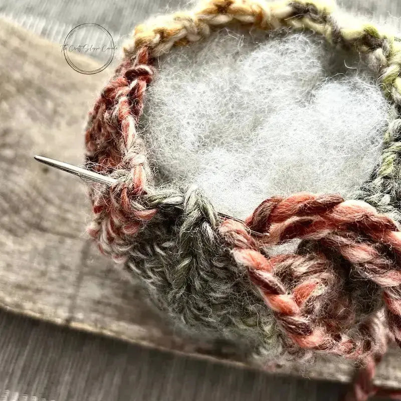 A close up of the top of the pumpkin, made from this crochet kit, to show the stuffing inside with a tapestry needle closing up the top.