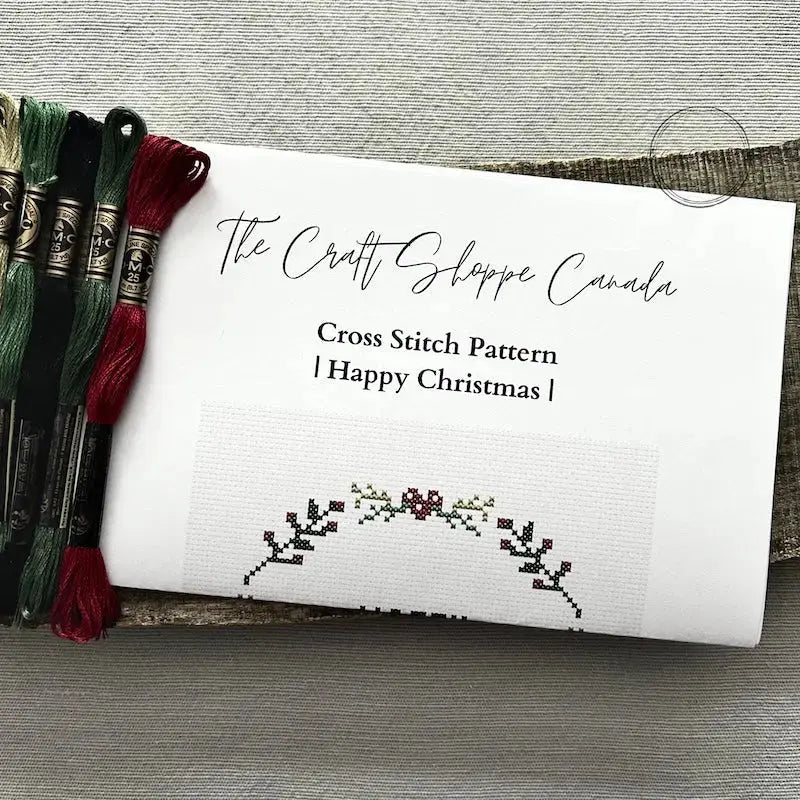 The pattern for this cross stitch kit is lying on a wooden board with DMC floss threads.