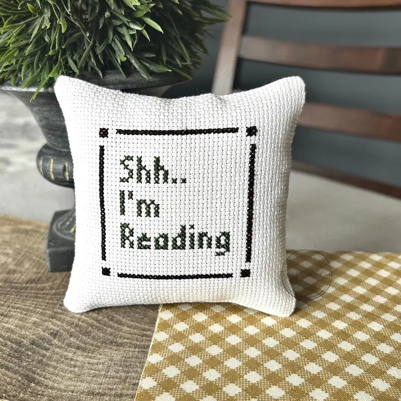 The finished pillow, made from this cross stitch kit, is sitting on a wooden board.