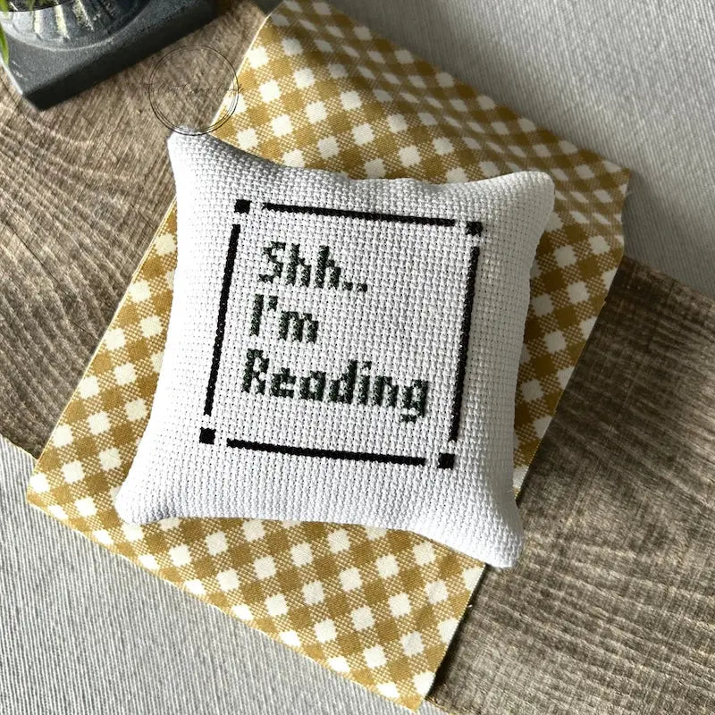 The finished pillow, made from this cross stitch kit, is sitting on a wooden board.