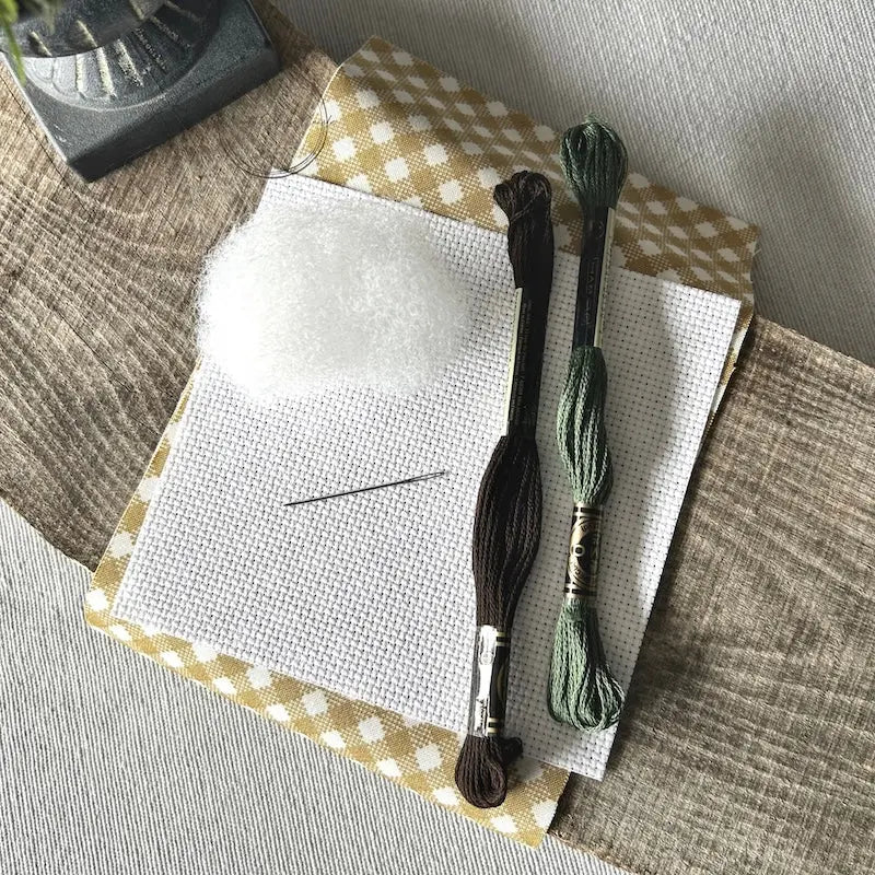 The supplies included in your cross stitch kit are sitting on a wooden board.