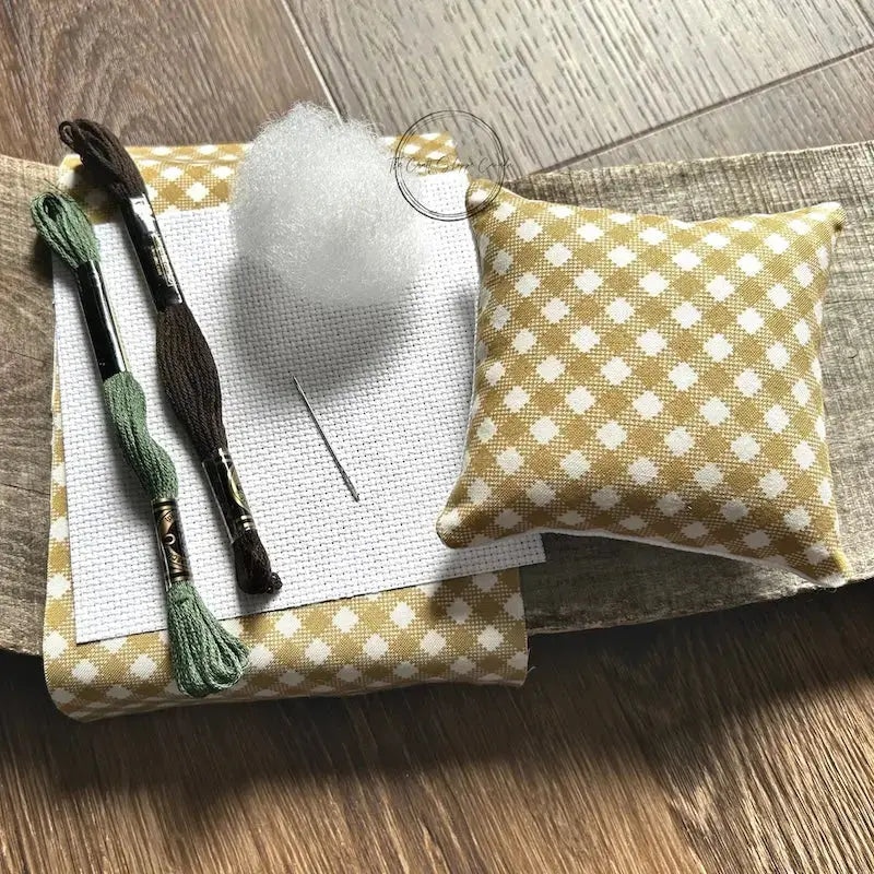 The supplies included in your cross stitch kit are sitting on a wooden board.