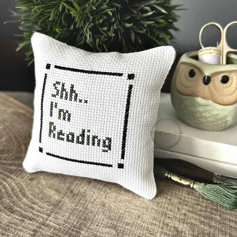 The finished pillow, made from this cross stitch kit, is sitting on a wooden board.