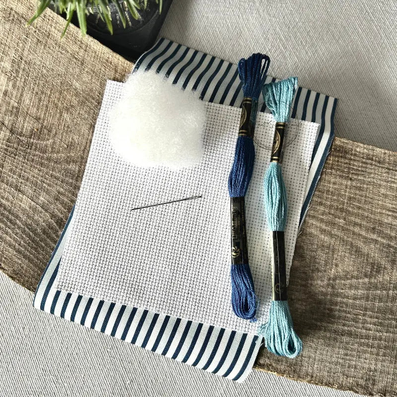 The supplies included in your cross stitch kit are sitting on a wooden board.