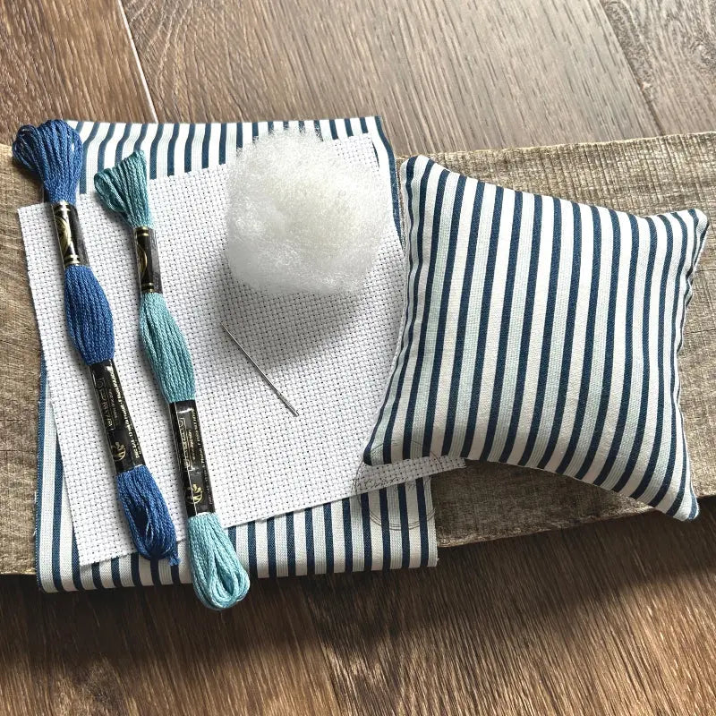 The supplies included in your cross stitch kit are sitting on a wooden board.