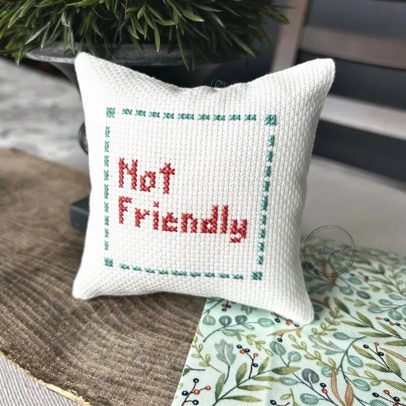 The finished pillow, made from this cross stitch kit, is sitting on a wooden board.