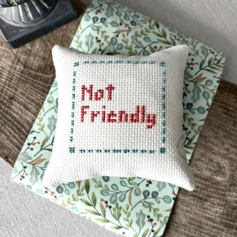 The finished pillow, made from this cross stitch kit, is sitting on a board.