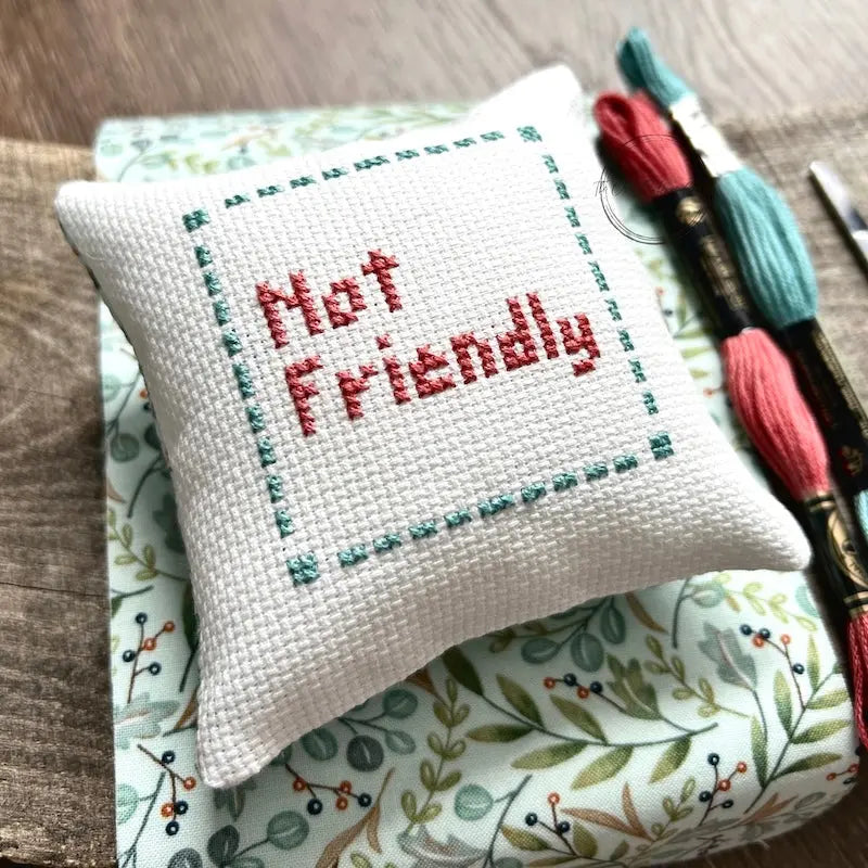 The finished pillow, made from this cross stitch kit, is sitting on a wooden board.