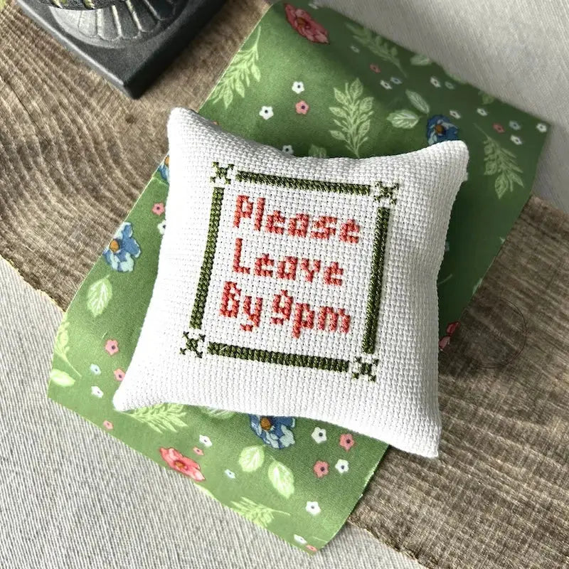The finished pillow, made from this cross stitch kit, is sitting on a board.