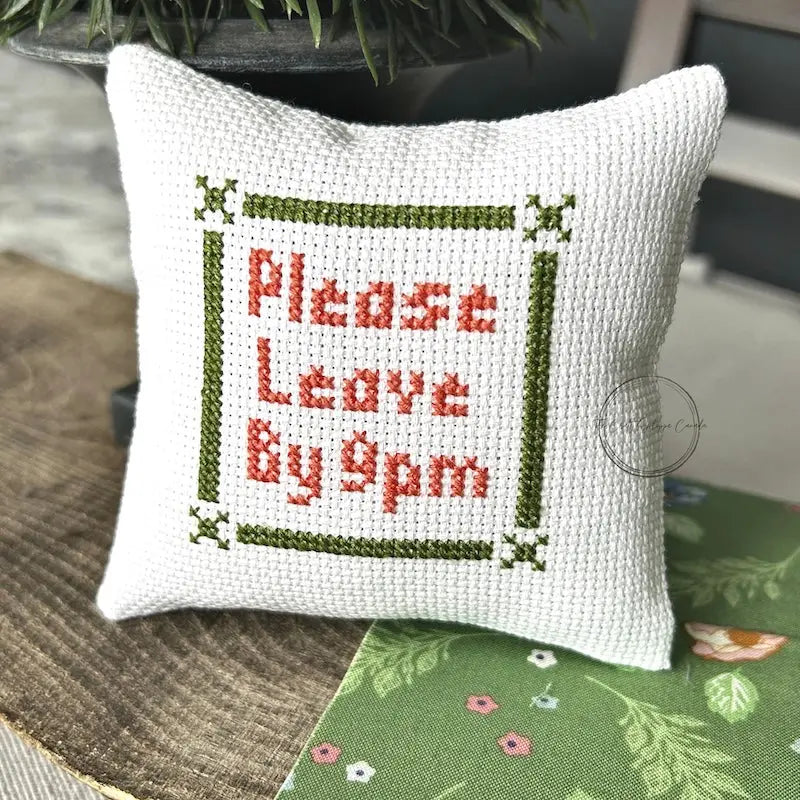 The finished pillow, made from this cross stitch kit, is sitting on a wooden board.