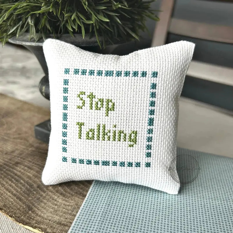 The finished pillow, made from this cross stitch kit, is sitting on a wooden board.
