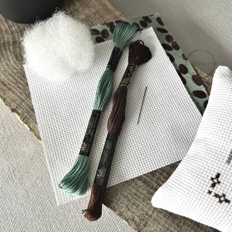 The supplies included in your cross stitch kit are sitting on a wooden board.