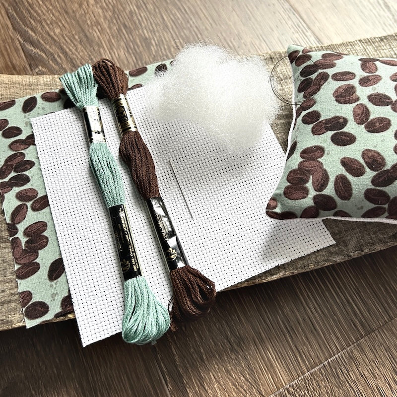 The supplies included in your cross stitch kit are sitting on a wooden board.