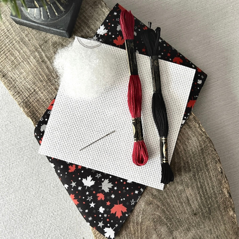 The supplies included in your cross stitch kit are sitting on a wooden board.