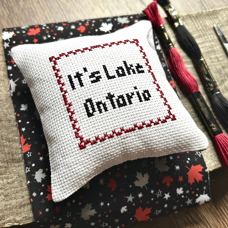 The finished pillow, made from this cross stitching kit, is sitting on a wooden board.