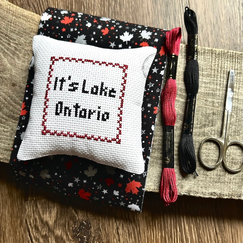 The finished pillow, made from this cross stitching kit, is sitting on a wooden board.
