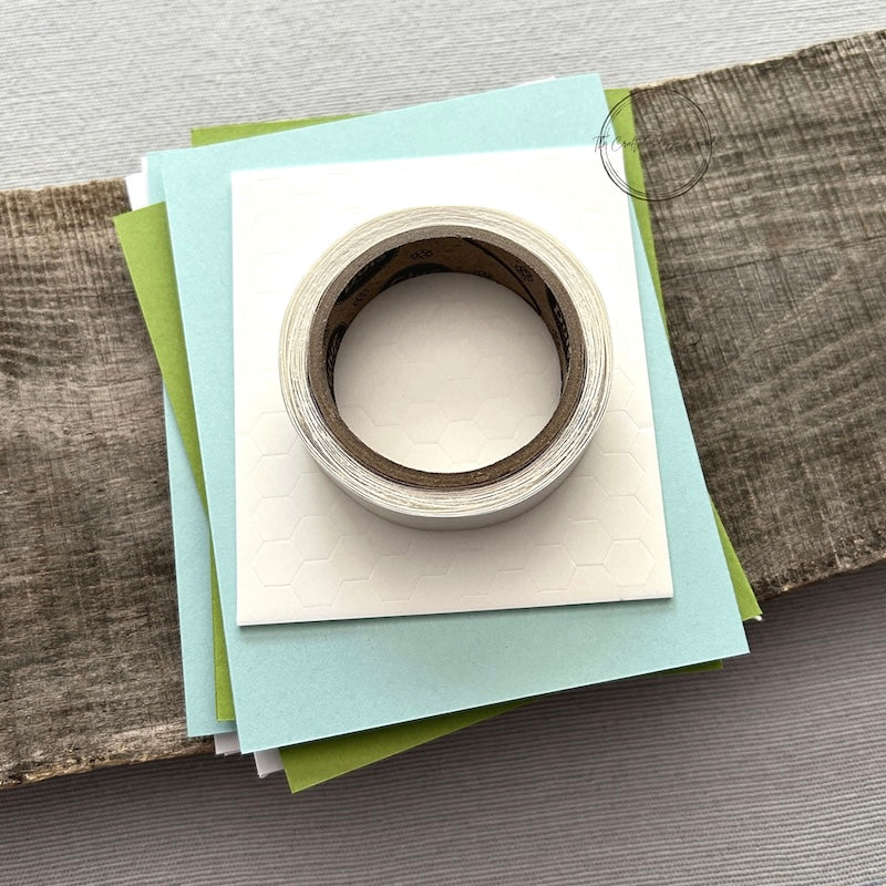 A roll of glue dots and a sheet of pop dots are sitting on a few blank cards. They are included in your card making kit.