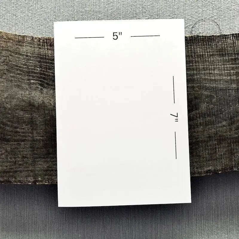 A blank card is sitting on a wooden board to show the measurements of the 5" x 7" card.