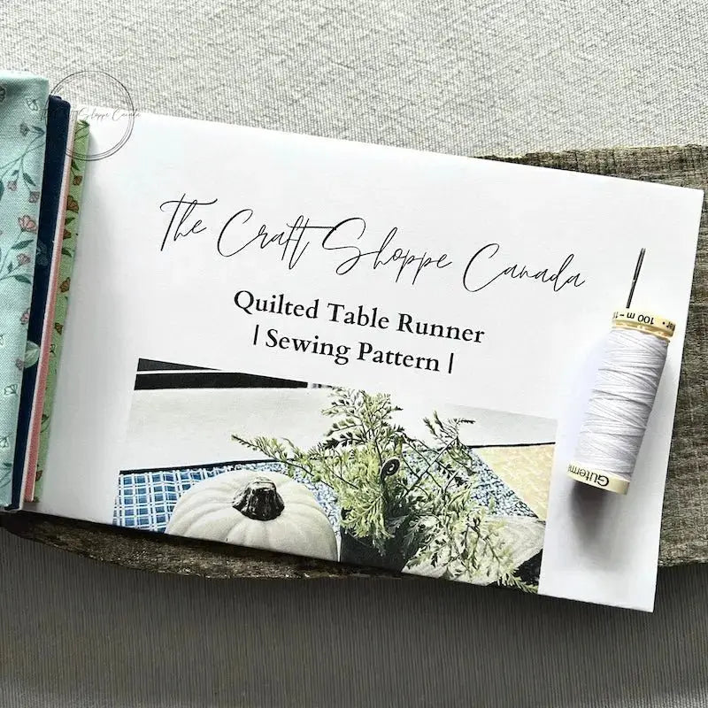 The pattern for this sewing kit is lying on a wooden board with fabric, a spool of thread and a hand sewing needle.