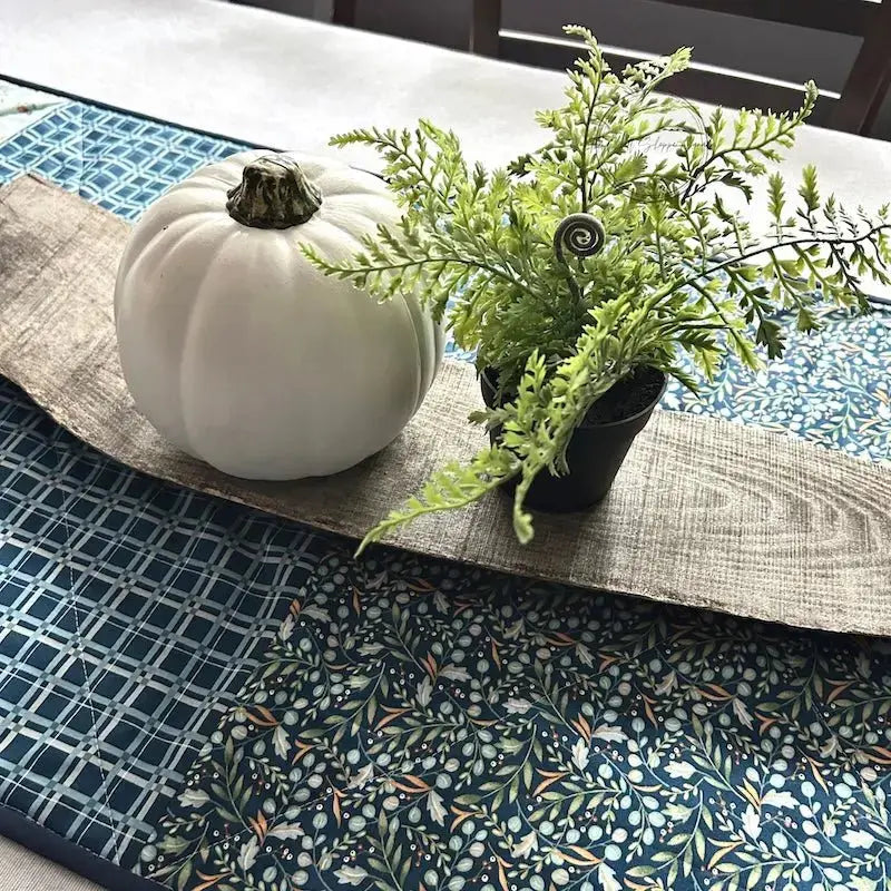 A quilted table runner, from this sewing kit, is lying on a wooden board on a table.