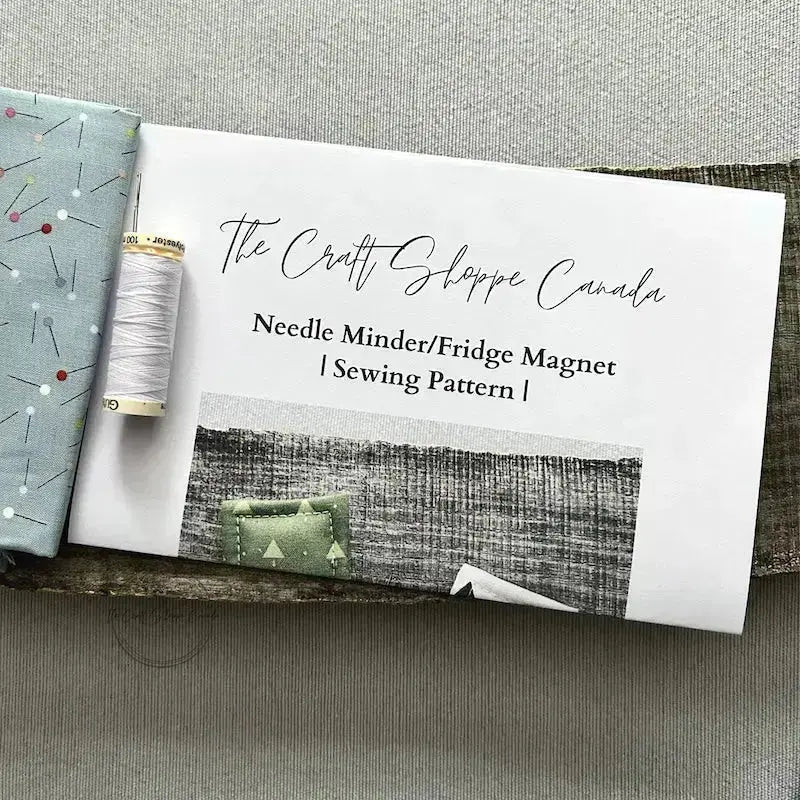 The pattern for this sewing kit is lying on a wooden board with fabric, a spool of thread and a hand sewing needle.