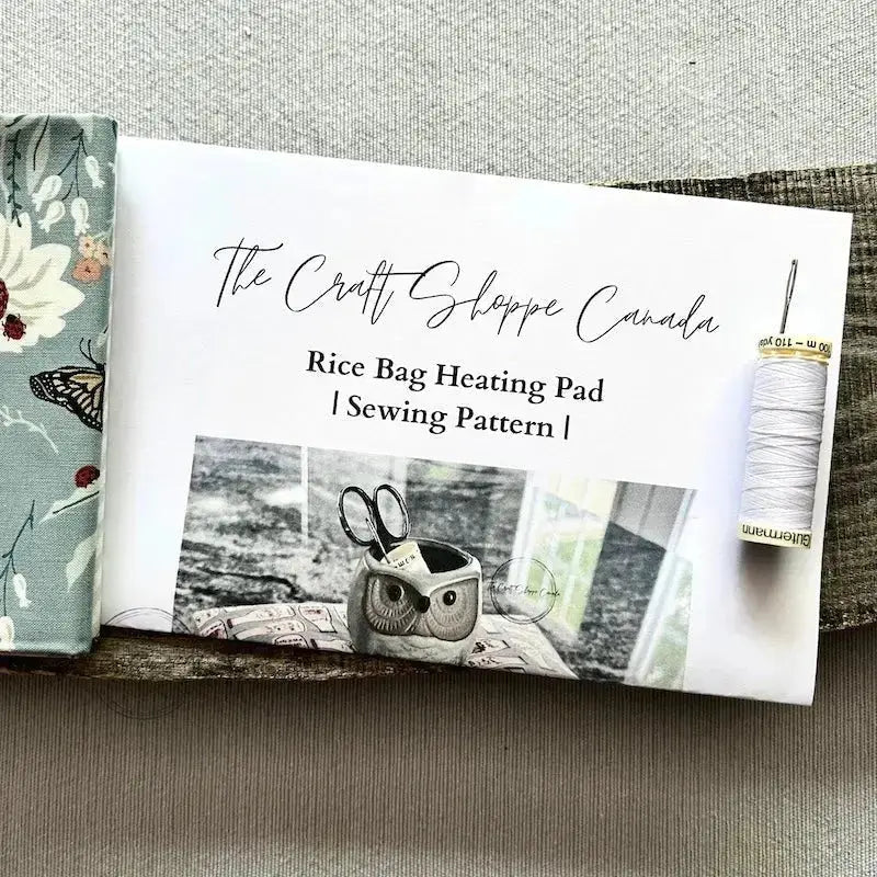 The pattern for this sewing kit is lying on a wooden board with fabric, a spool of thread and a hand sewing needle.