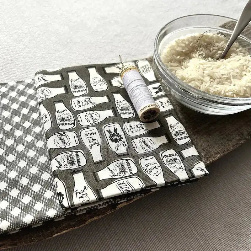 Fabric from this sewing kit, is sitting on a wooden board beside a bowl of rice.