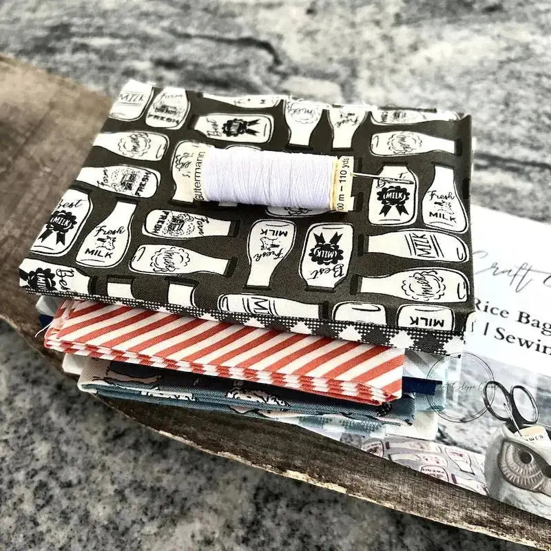 Fabric from this sewing kit, is sitting on a wooden board with a copy of the sewing pattern, a spool of white thread and a hand sewing needle.