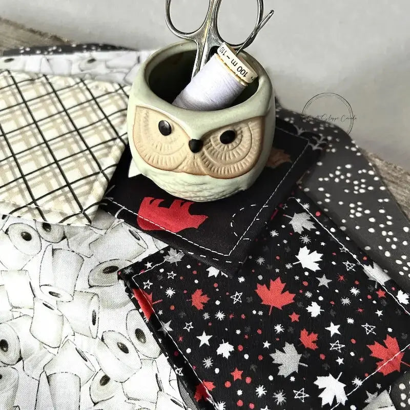 The fabric used in this sewing kit, along with some finished coasters are lying on a wooden board with fabric, scissors and a spool of thread.