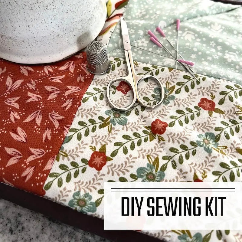 A DIY sewing kit for a pot holder trivet. The pot holder is sitting on a wooden board with a pair of scissors, a thimble, and sewing pins.