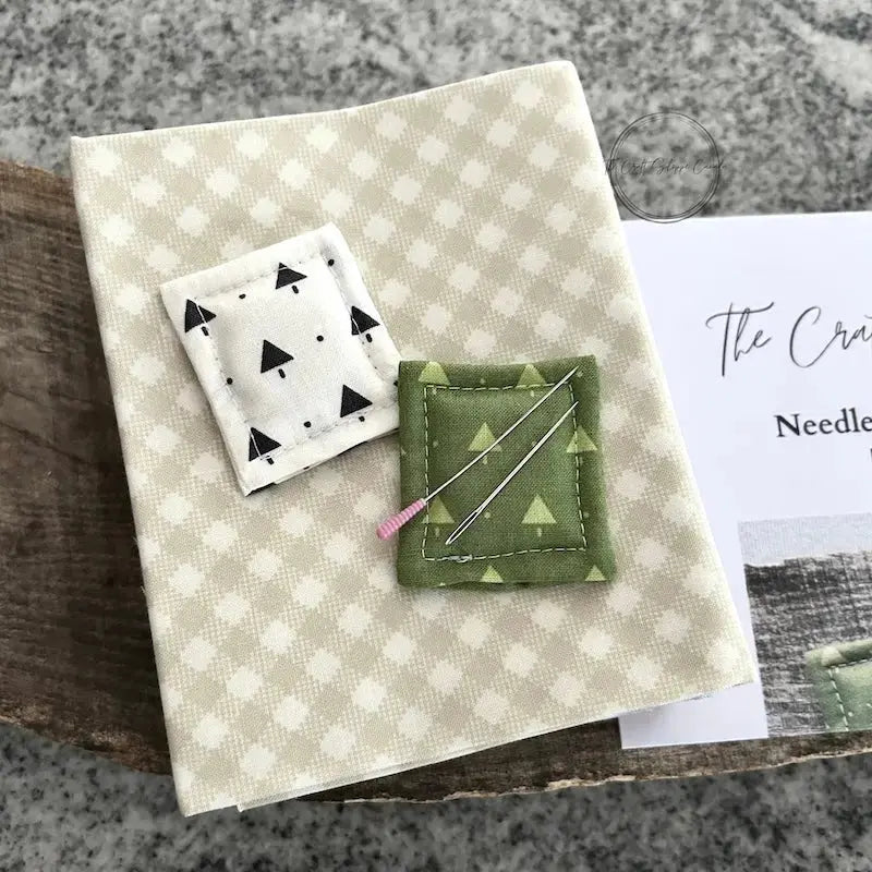 The 2 needle minders, made from this sewing pattern, are sitting on a stack of fabric, with sewing pins.