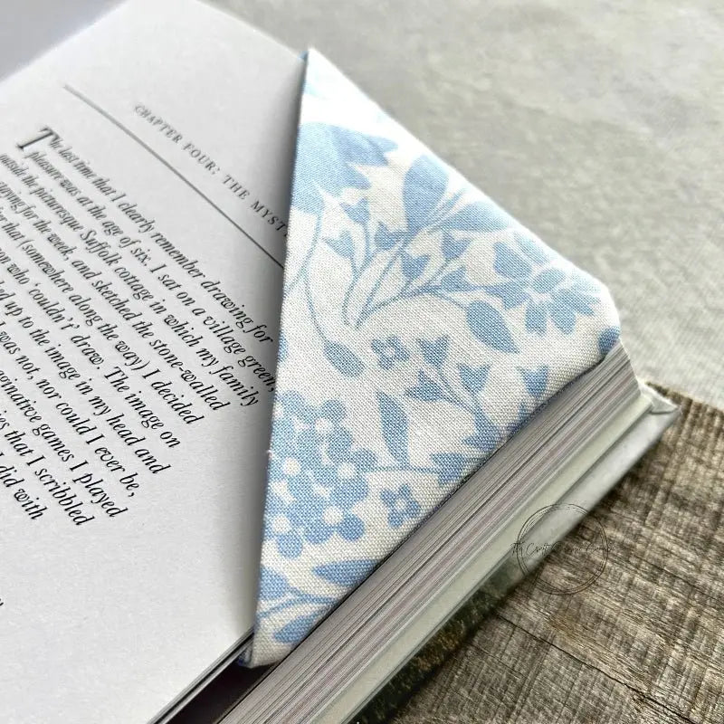 A corner bookmark, made from this sewing pattern, is sitting on the corner of pages from a book.