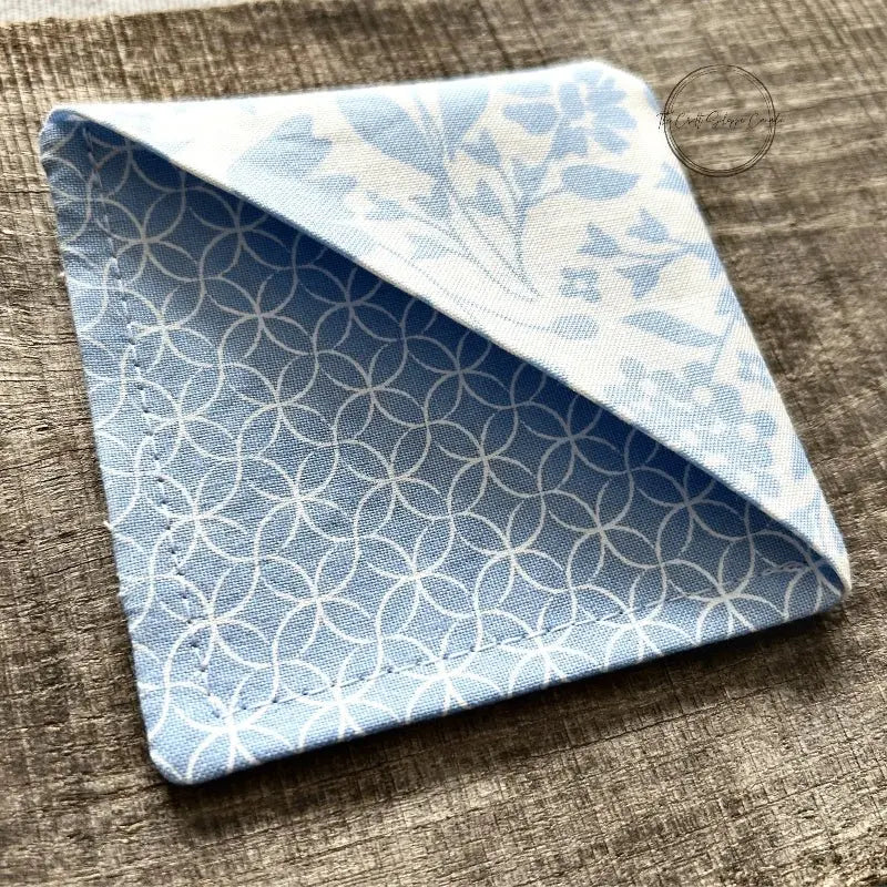 A corner bookmark, made from this sewing pattern, is sitting on a wooden board.